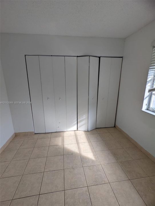 Room featuring neutral ceramic tile flooring, a multi-panel folding closet door, and a single window with horizontal blinds