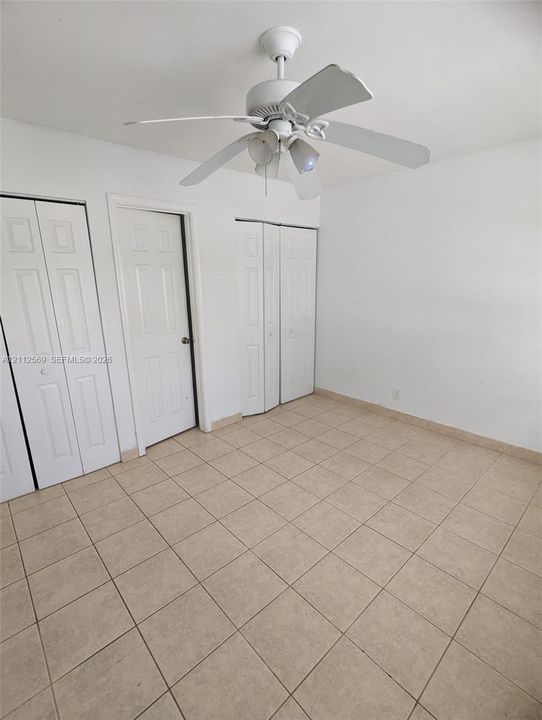 Ceramic tile flooring, white four-panel interior doors, bi-fold closet doors, and a ceiling-mounted light fixture with a fan
