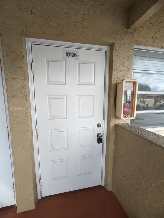 White six-panel entry door with a dedicated address plate and metal hardware, set against a textured stucco exterior wall