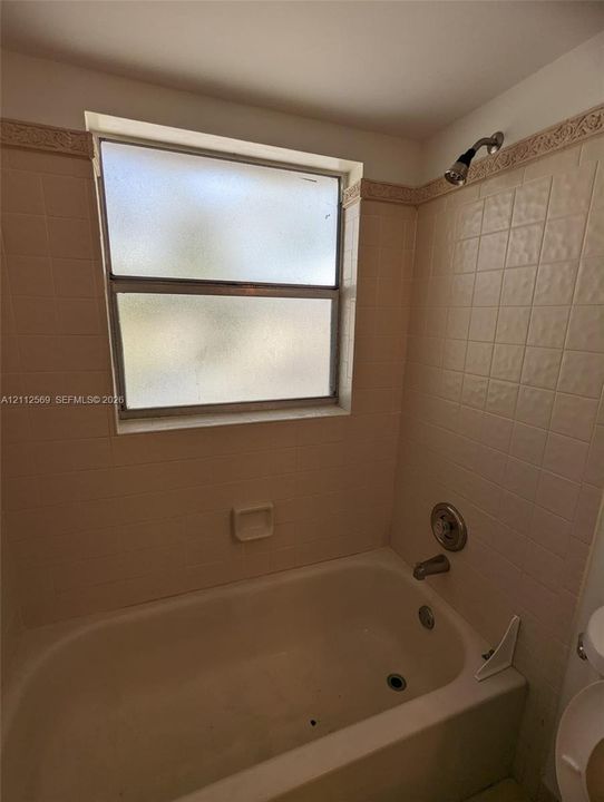 Bathtub and shower combination featuring tiled surround, built-in soap niche, frosted glass window, and chrome plumbing fixtures