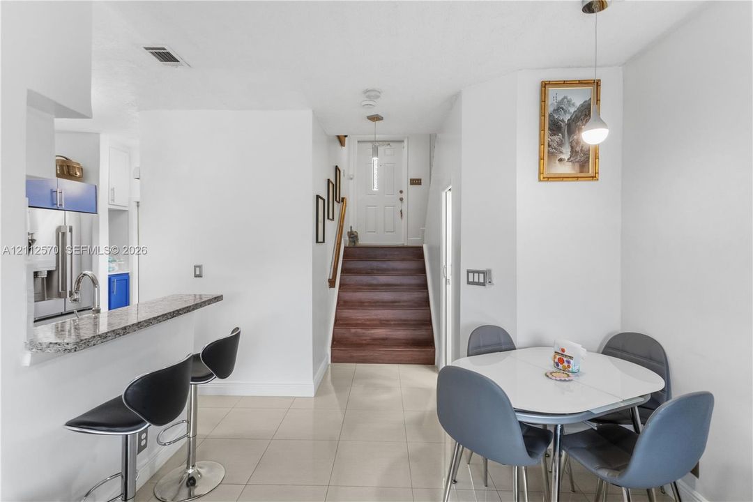 Open-concept kitchen area featuring a stone-topped breakfast bar, tile flooring, and stairs with wood-finish treads leading to an exterior entryway with a glass-paneled door