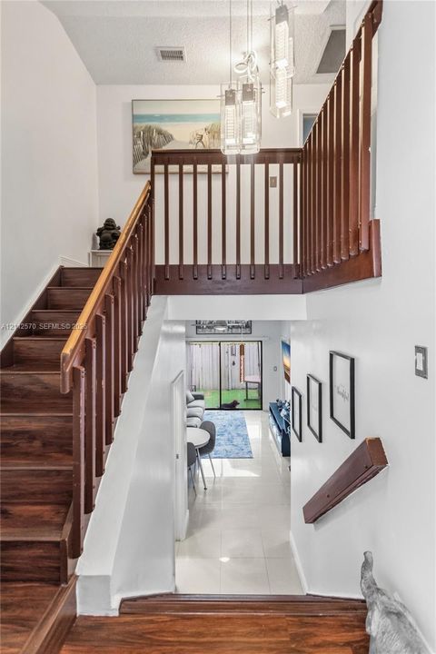 Entryway featuring a wood-finished staircase with matching balustrades, polished tile flooring, and a multi-pendant light fixture