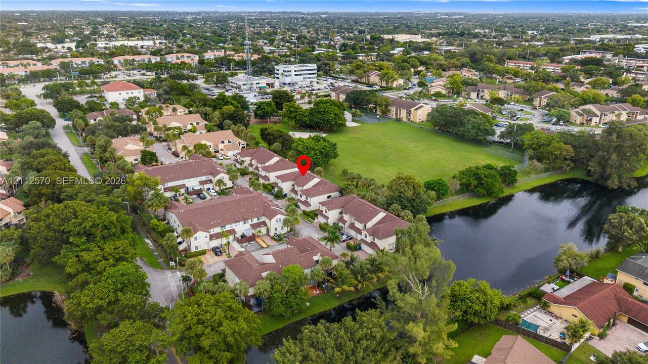Aerial perspective of residential complex featuring tile roofing, mature landscaping, and proximity to an expansive grass common area and water features