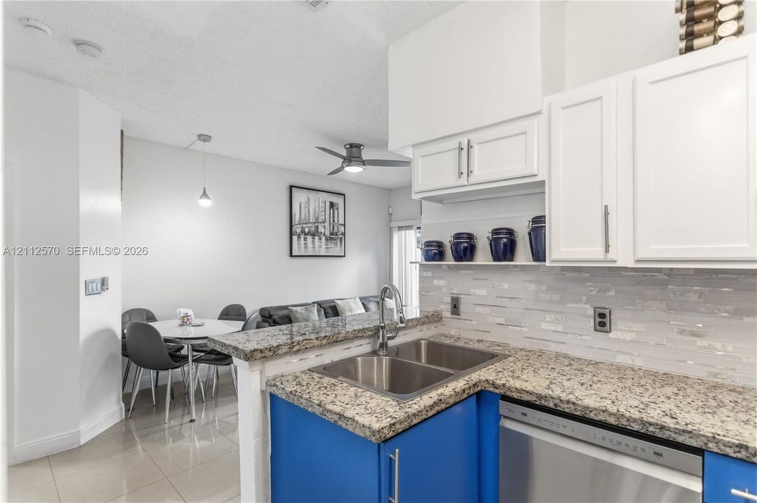 Kitchen featuring stone countertops, white upper cabinetry, blue lower cabinetry, stainless steel double-basin sink, and mosaic tile backsplash