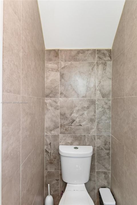 Full-height, large-format tile surround with stone-texture finish and white dual-flush toilet