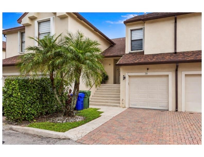Stucco exterior featuring an attached garage, paver driveway, and concrete stairs leading to the entryway
