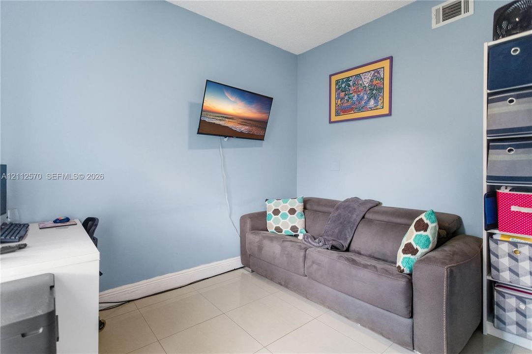Room featuring light-toned neutral tile flooring and wall-mounted television hardware