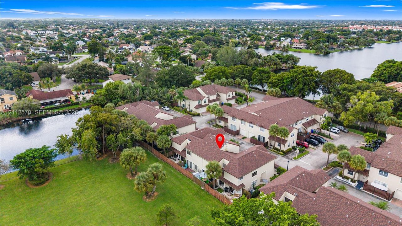 Aerial perspective of a multi-unit property featuring a shingled roof, stucco exterior, and placement bordering a canal and grassy common area
