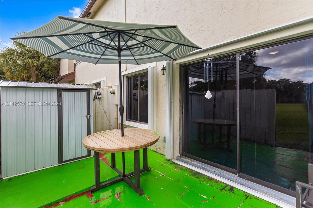 Exterior patio with painted concrete flooring, sliding glass door, and a detached metal storage shed