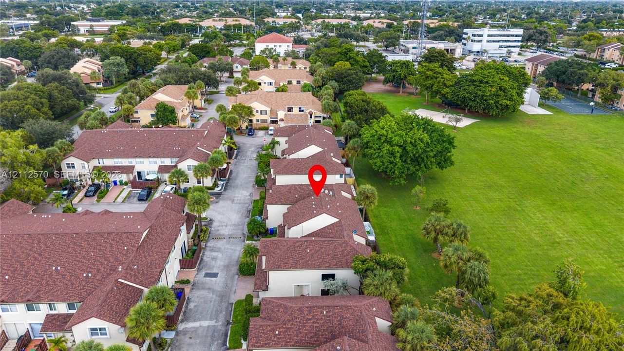 Aerial perspective highlighting a multi-unit residential property with shingled roofing, paved driveway access, and mature landscaping bordering an expansive open green space