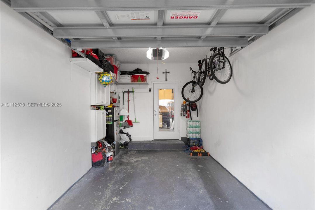 Enclosed garage featuring painted concrete flooring, white cabinetry, overhead lighting, and a single pedestrian entry door with glass paneling