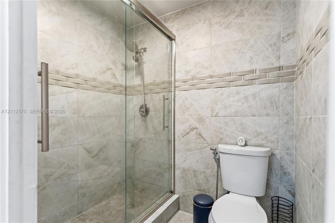 Walk-in shower with a glass enclosure, brushed nickel handheld showerhead, floor-to-ceiling stone-patterned tile, and decorative horizontal tile accent border