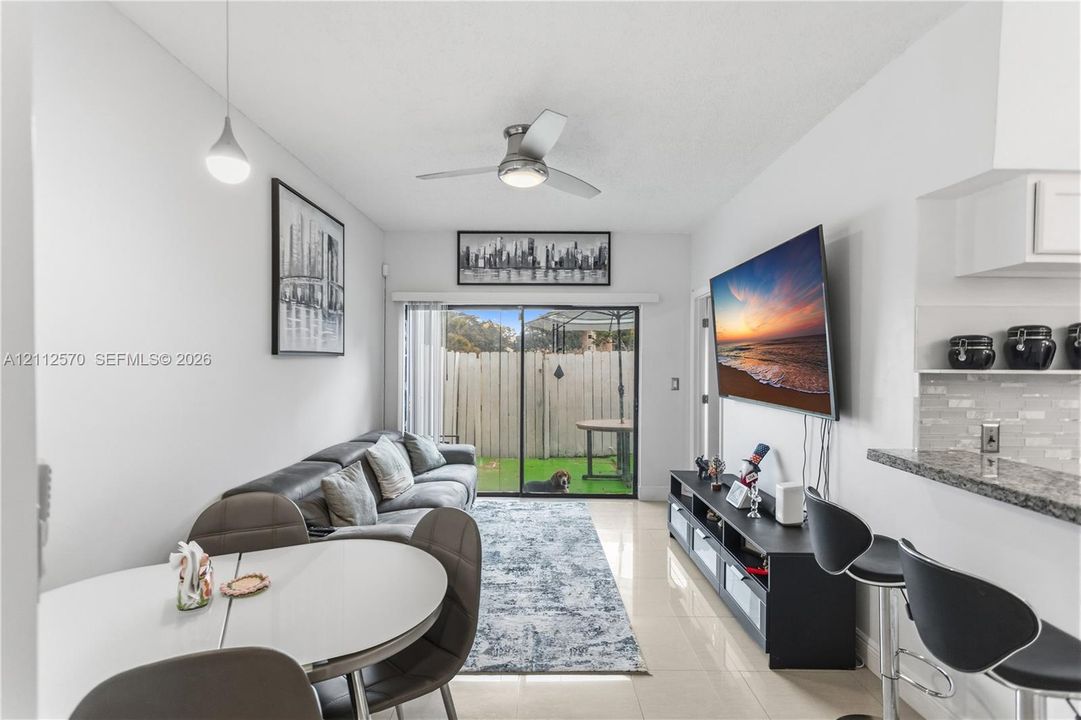 Neutral-toned tile flooring, ceiling-mounted fan with integrated light, sliding glass doors, and a stone-surface breakfast bar