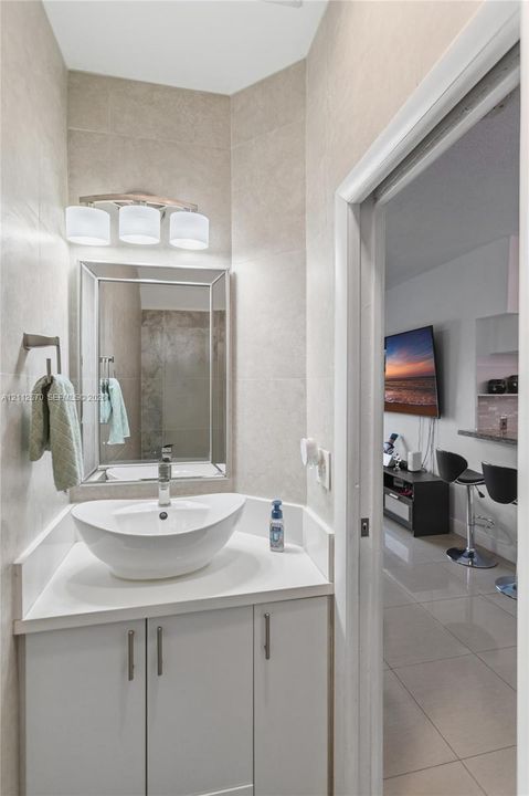 Bathroom featuring a white vanity cabinet, solid-surface countertop, vessel sink with a chrome faucet, tri-light fixture, and framed wall mirror