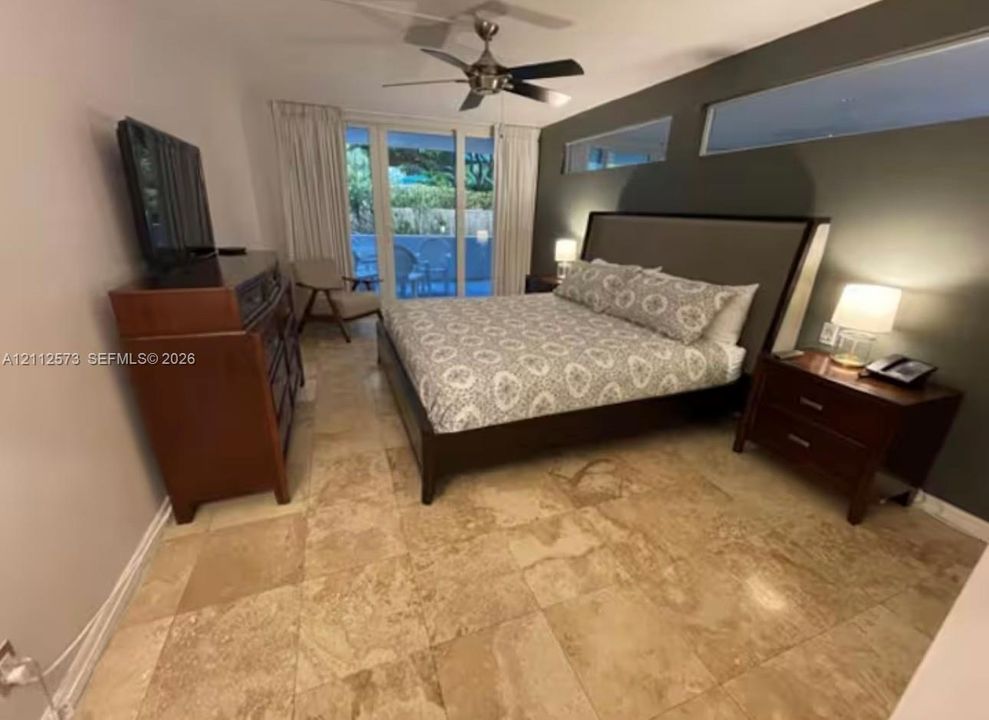Natural stone flooring, ceiling fan with light fixture, accent wall, and sliding glass patio door