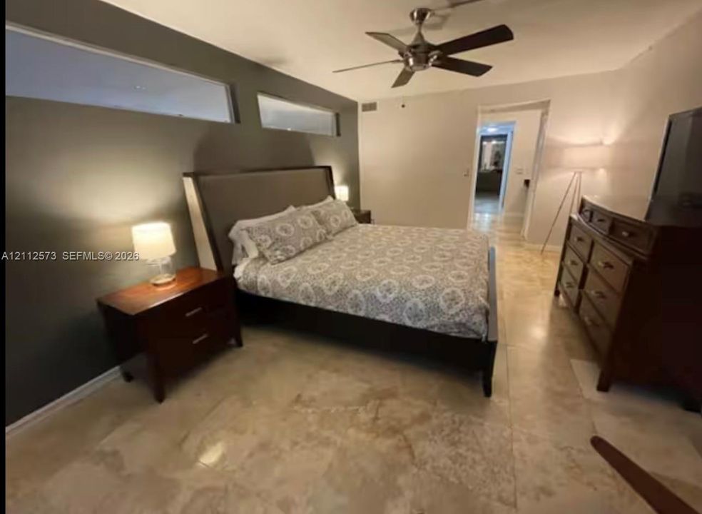 Room featuring large-format light-toned stone tile flooring, high-contrast dark accent wall with transom windows, and a multi-blade ceiling fan