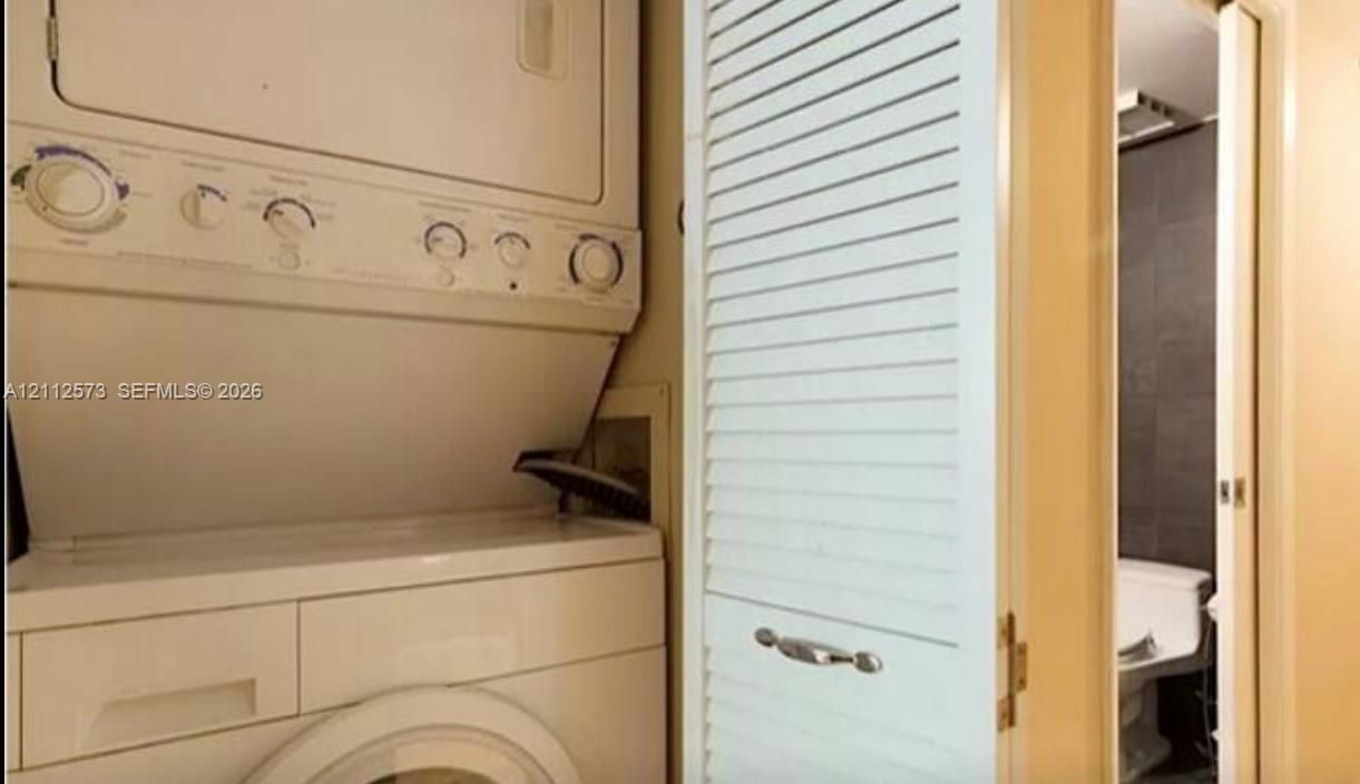 Stacked laundry appliance unit featuring a white finish, enclosed by a louvered bi-fold door with metal hardware