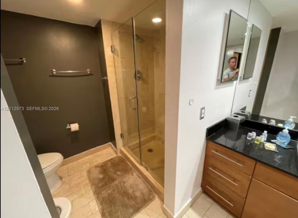 Bathroom featuring a glass-enclosed shower with tile surround, wood-finish cabinetry, a dark stone countertop, and recessed lighting