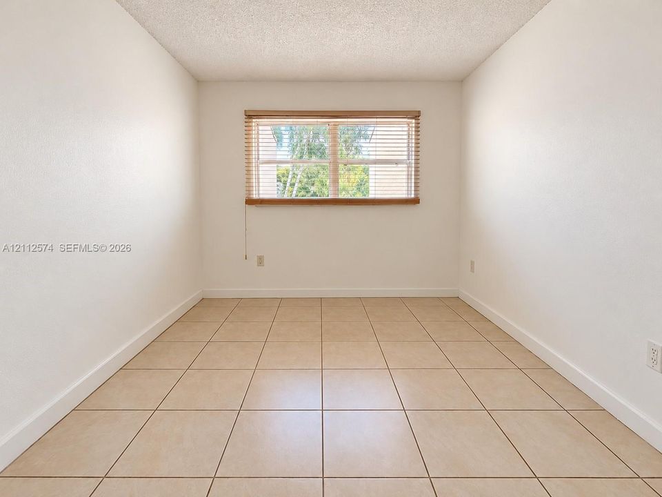 Neutral-toned tile flooring, textured ceiling, and a large central window with horizontal slat blinds