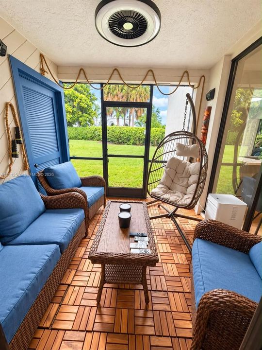 Enclosed patio featuring wood-finish deck tiling, screened wall panels, a door providing exterior access, and a flush-mount circular ceiling fixture