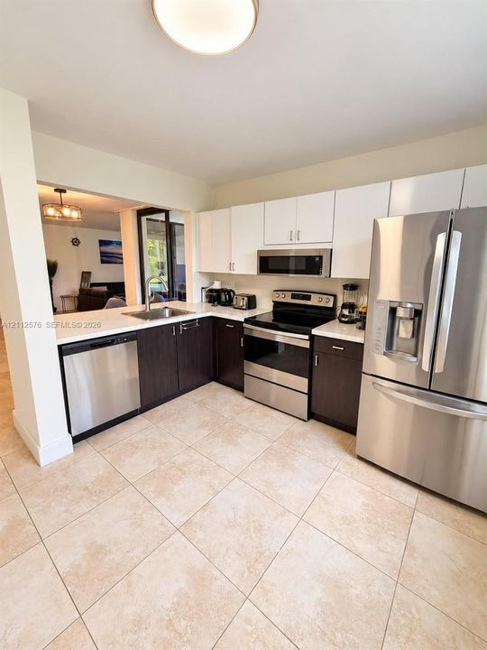 Kitchen featuring two-tone cabinetry, stainless steel appliances, light-toned countertops, and tile flooring