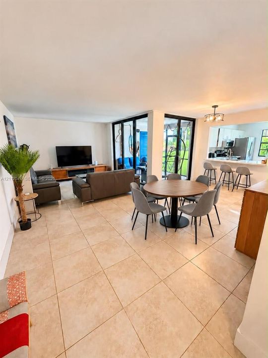 Open-concept living space featuring large-format tile flooring, expansive floor-to-ceiling glass sliding doors, and a kitchen pass-through with an integrated breakfast bar