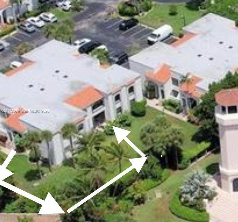 Aerial perspective of low-rise residential structures featuring light-toned stucco facades, multi-pitched roofs with terra cotta accents, and expansive landscaped grounds with mature palm trees