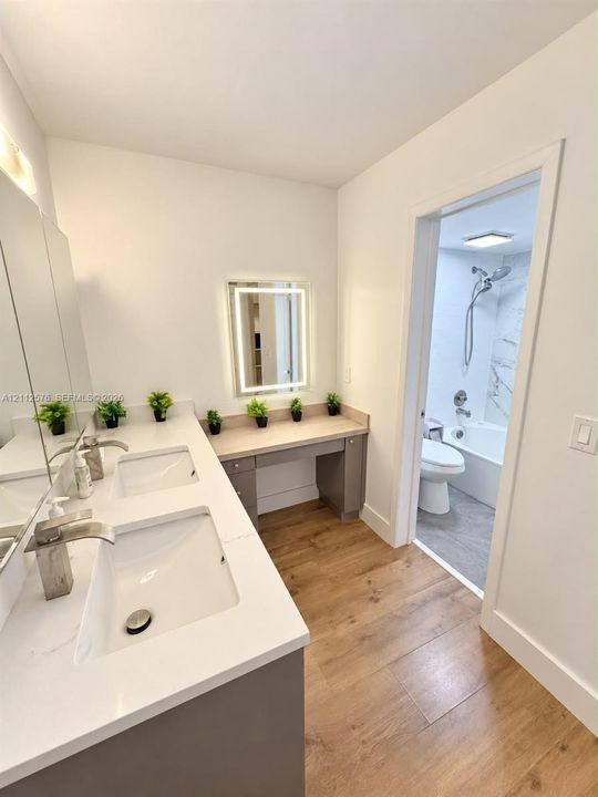Double vanity with integrated sinks, quartz countertops, modern cabinetry, LED-backlit mirror, and wood-finish flooring