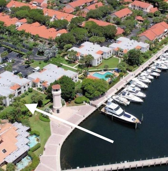 Aerial perspective of a multi-unit residential property featuring direct water access, a dedicated deep-water boat slip, a prominent decorative lighthouse structure, and manicured grounds