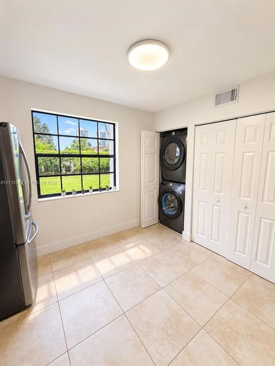 Large-format tile flooring, industrial-style grid window, built-in stacked laundry appliance, and white six-panel closet doors