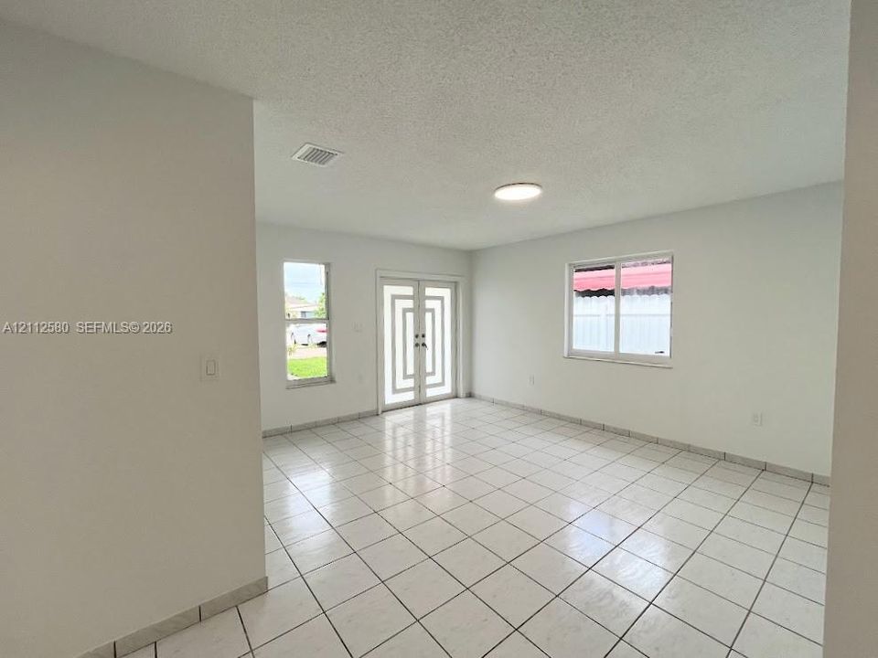 Interior space featuring white tile flooring, neutral walls, double front doors with geometric glass detailing, and dual-pane windows