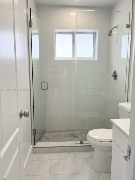 Walk-in shower featuring a frameless glass enclosure, polished chrome fixtures, white subway-style wall tile, and patterned tile flooring