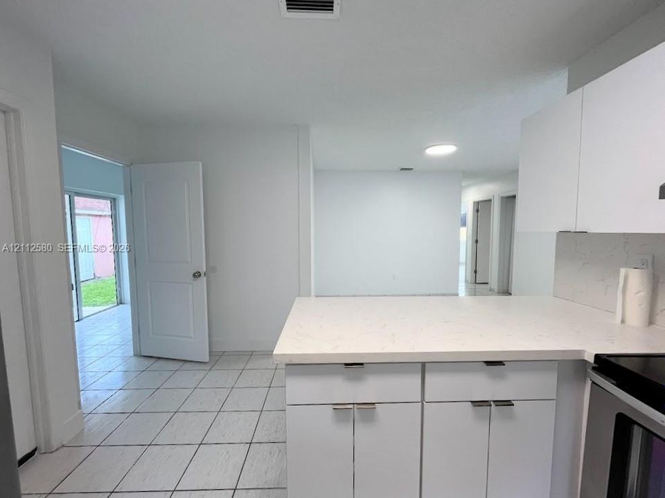 Kitchen featuring white cabinetry, light-toned stone-finish countertops, tile flooring, and integrated stainless steel appliances