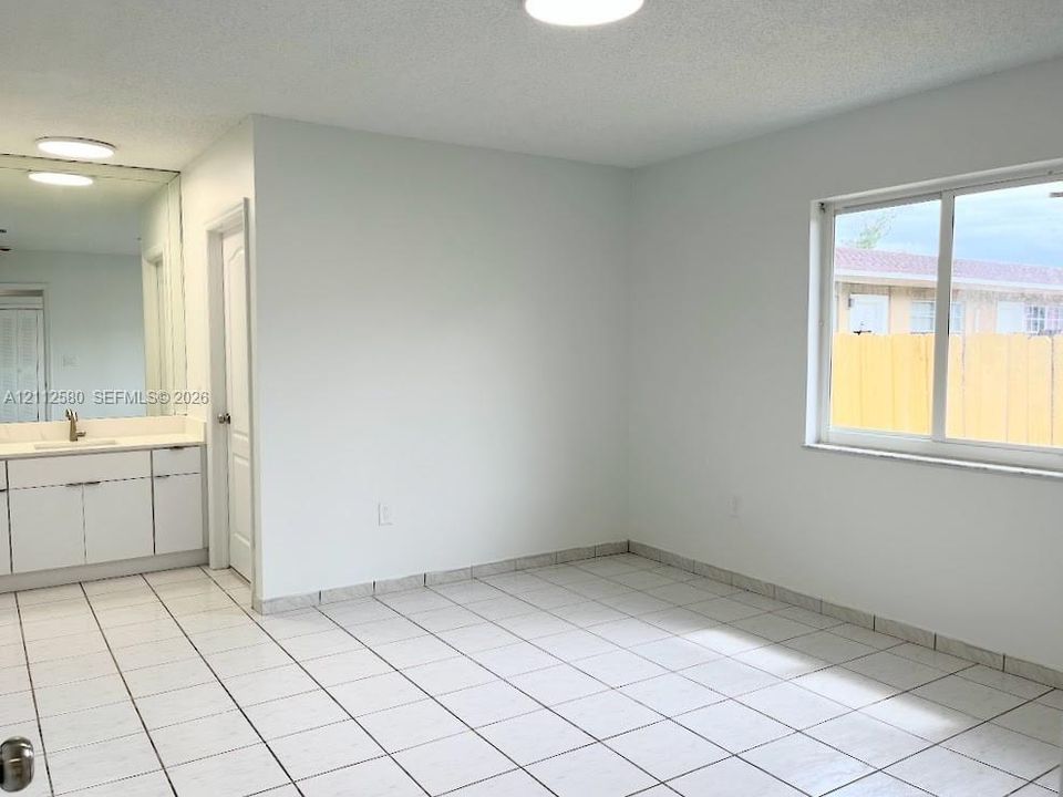 White tile flooring, single-panel interior door, large wall-mounted mirror, white vanity cabinetry, and a horizontal sliding window