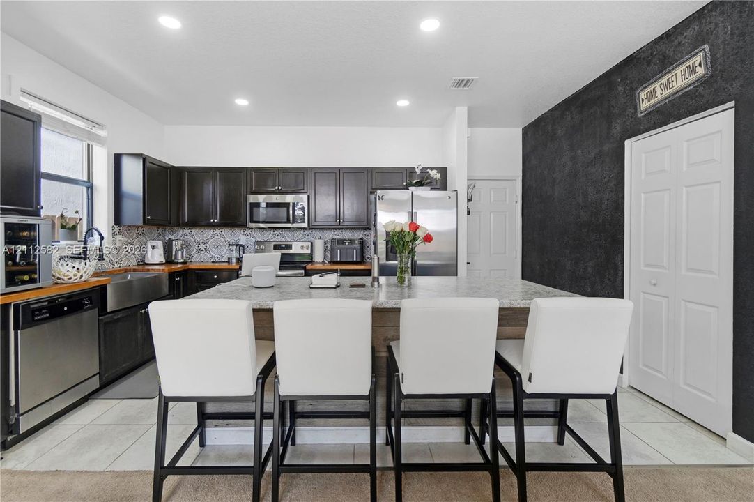Kitchen featuring dark wood cabinetry, stainless steel appliances, patterned tile backsplash, oversized stone-topped island, and recessed lighting