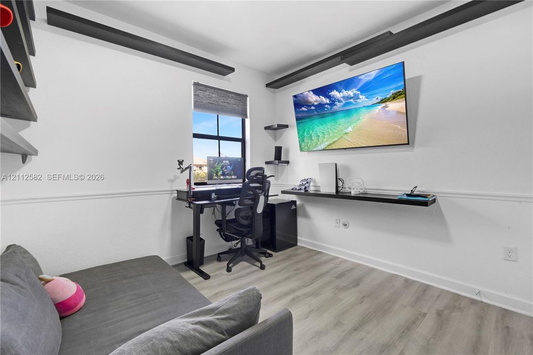 Room featuring wood-finish flooring, decorative ceiling beams, built-in shelving, and a wall-mounted floating desk