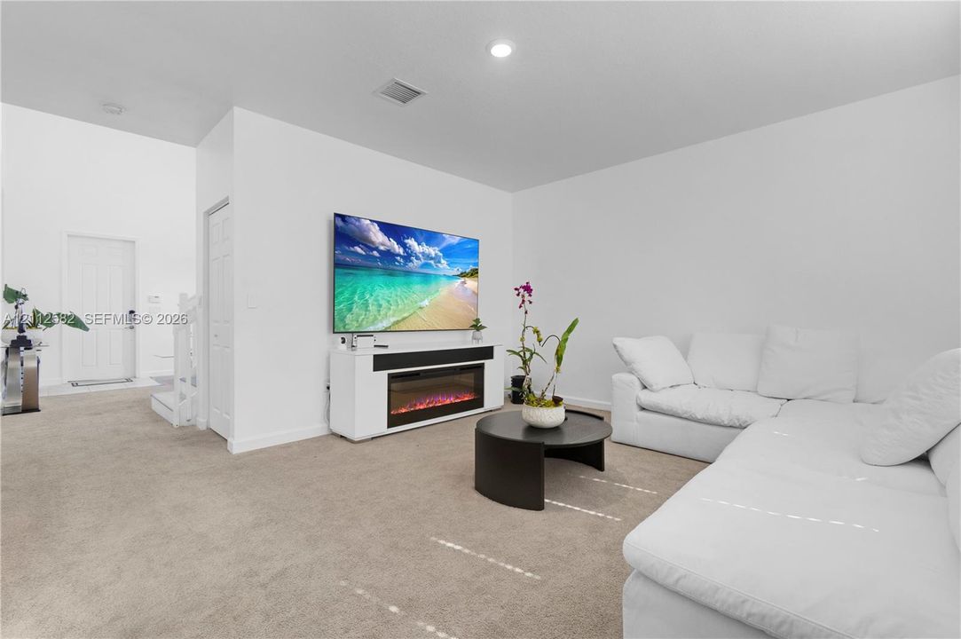 Living area featuring neutral carpeting, recessed ceiling lighting, and a built-in media console with an integrated electric fireplace