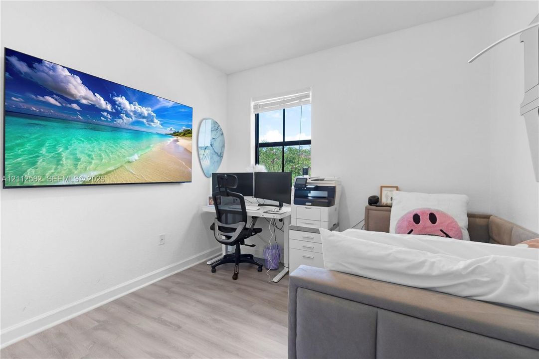Neutral-toned wood-finish flooring, white walls, and a window featuring a black frame