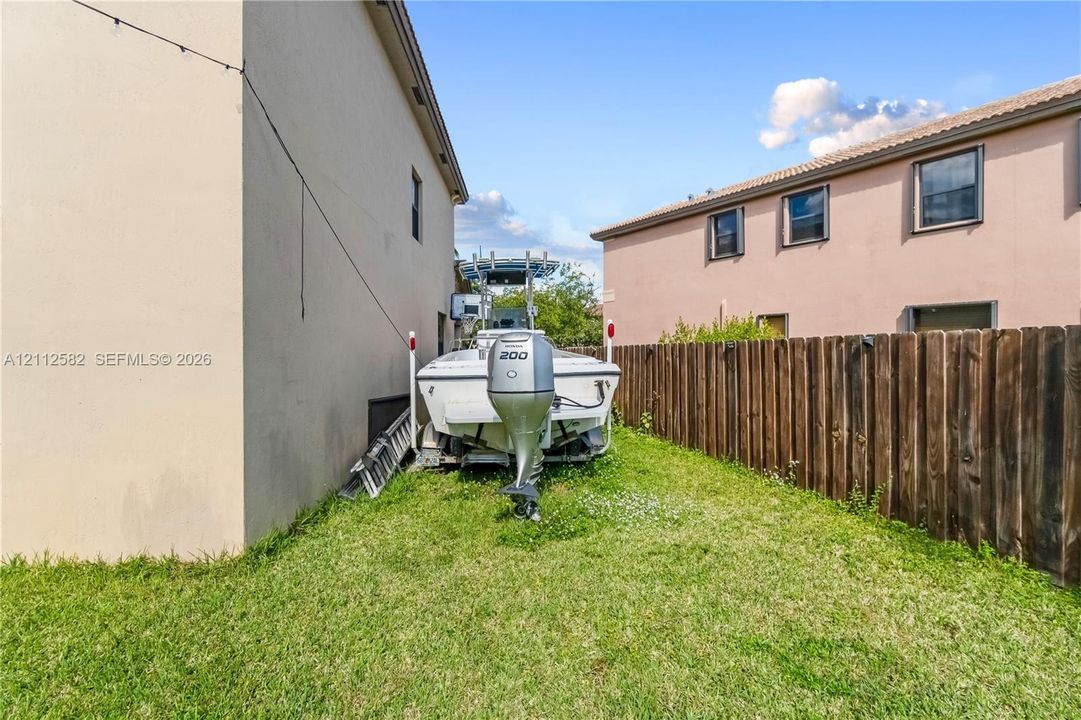 Side yard area featuring grass lawn, perimeter wood fence, and stucco exterior walls