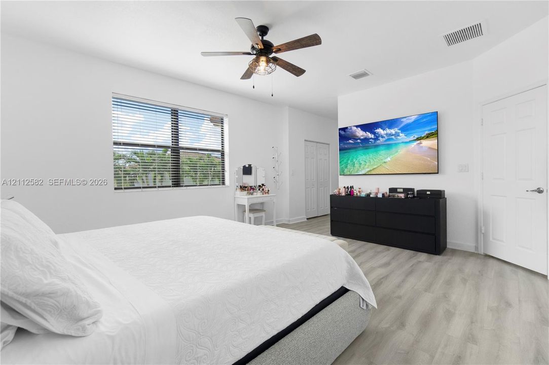 Neutral-toned interior space featuring wood-finish flooring, a multi-blade ceiling fan with integrated lighting, and a multi-pane window