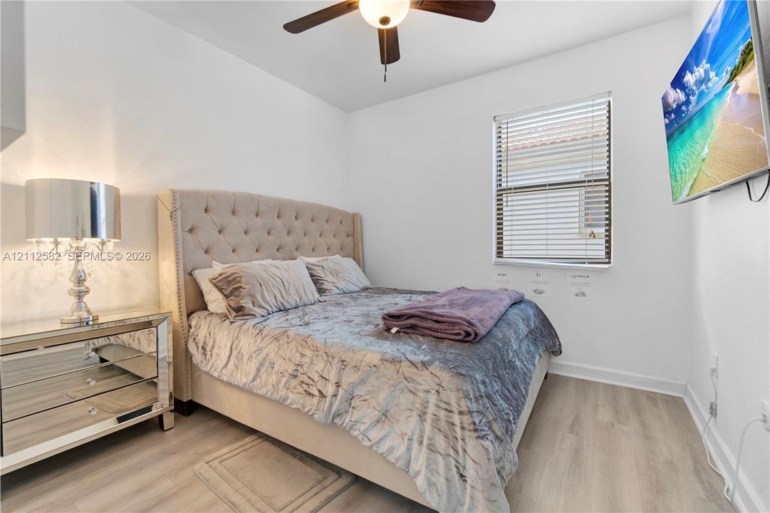 Neutral-toned wood-finish flooring, ceiling fan with integrated lighting, and horizontal window blinds