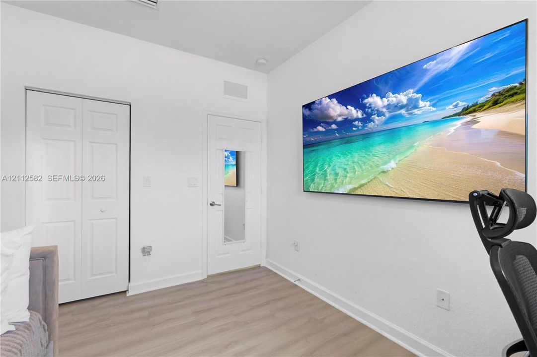 Interior room featuring wood-finish flooring, white walls, a double-door closet, and a single-panel door with an integrated mirror