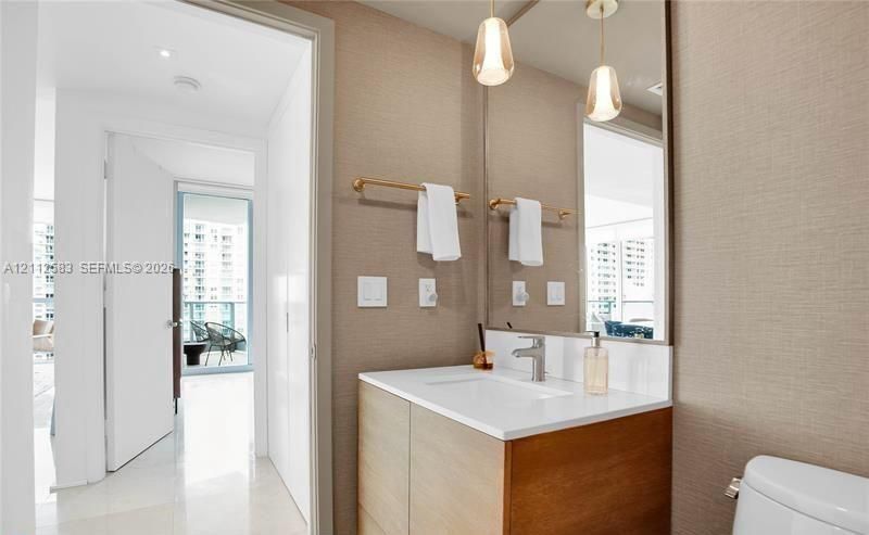 Bathroom vanity featuring a wood-finish cabinet, white surface, metallic faucet, dual glass pendant lights, and a floor-to-ceiling mirror