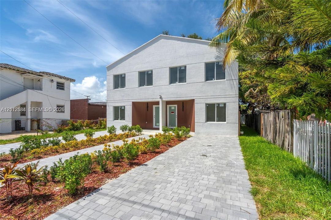 Two-story exterior featuring a light-toned stucco facade, dual recessed entryways, rectangular windows, and a paved stone driveway
