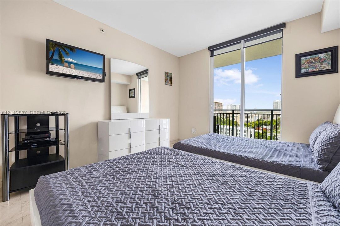 Floor-to-ceiling sliding glass door, private exterior balcony with metal railing, and neutral stone-finish flooring