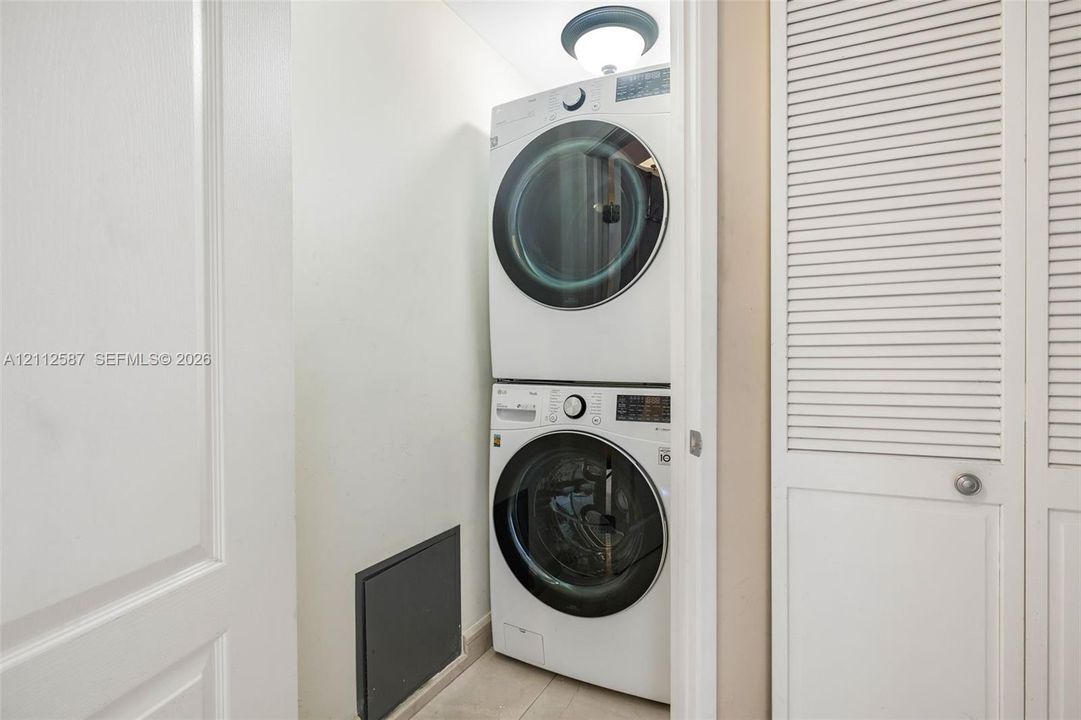 Stacked front-load laundry unit featuring a circular ceiling-mounted light fixture and white louvered closet doors