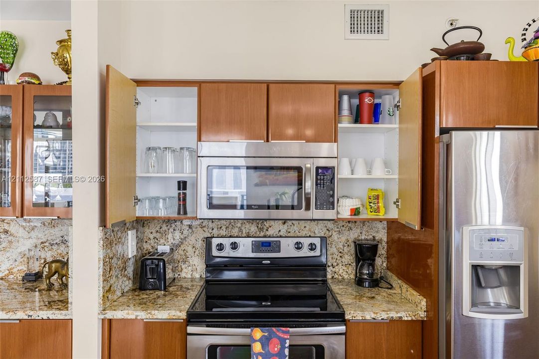 Kitchen featuring wood-finish cabinetry, natural stone countertops, a stainless steel built-in microwave, a stainless steel range, and a stainless steel refrigerator