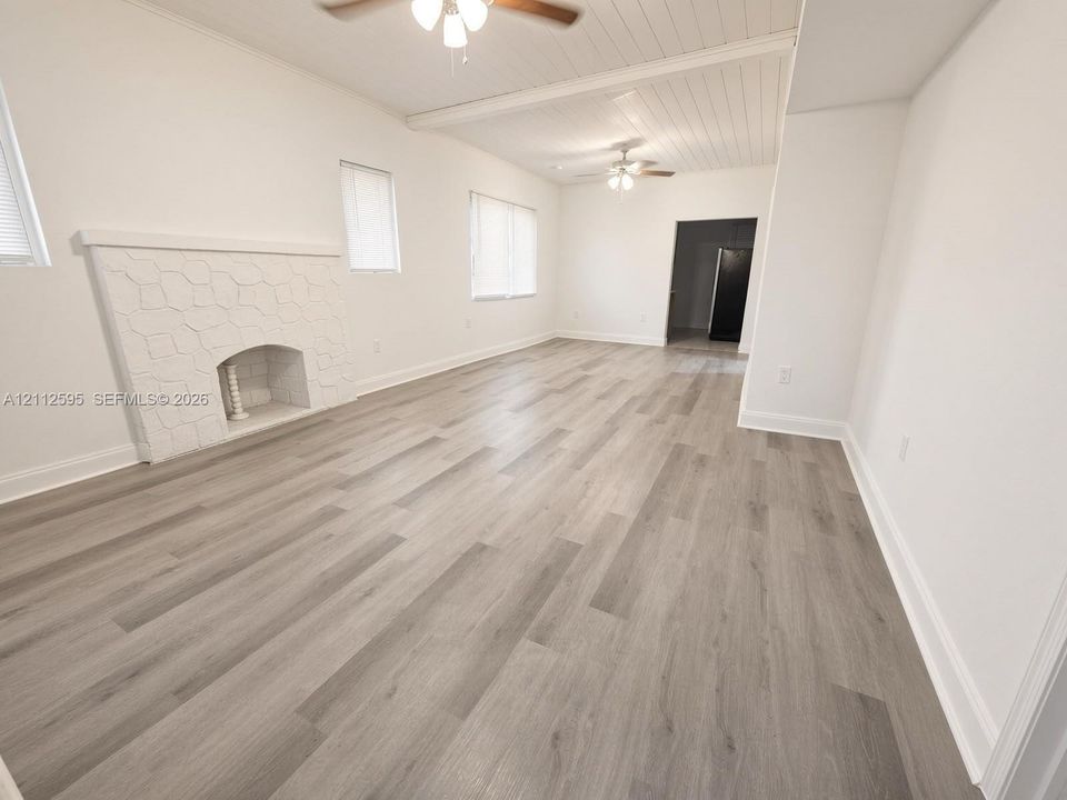 Open floor plan featuring wood-finish flooring, a textured fireplace surround, beadboard ceiling detailing, and dual ceiling fans