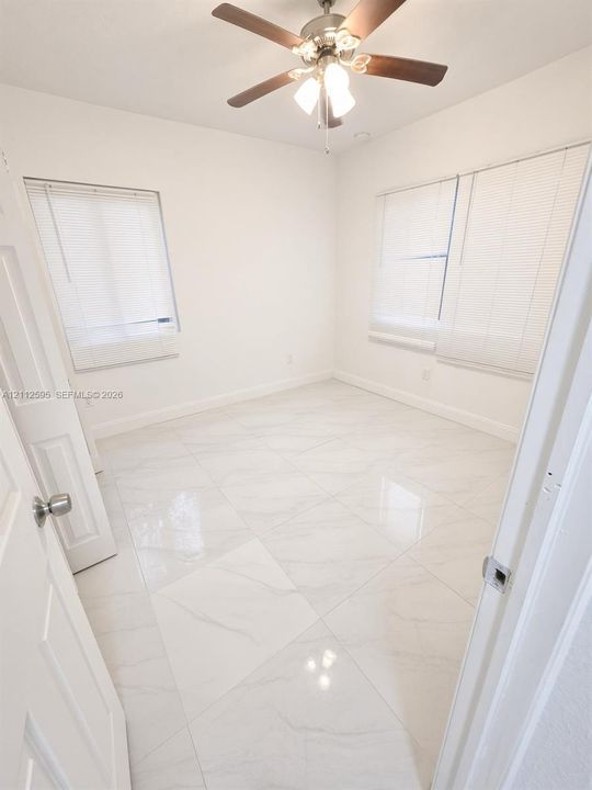 Large-format tile flooring with a light veined finish, multi-paneled interior doors, and a ceiling-mounted light fixture with a multi-blade fan