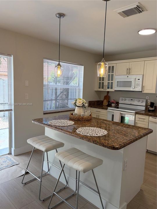 Kitchen featuring a center island with a granite countertop, off-white cabinetry, glass-front upper cabinet doors, and dual glass pendant light fixtures